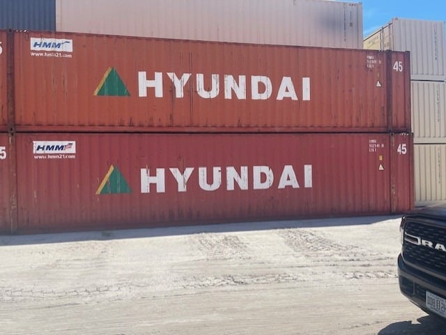 Shipping containers with Hyundai logo stacked at a port facility.
