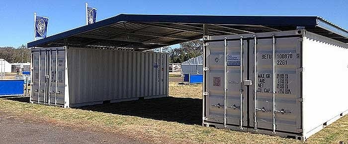 Shipping containers with a metal roof in an open field, used for storage and protection from weather.