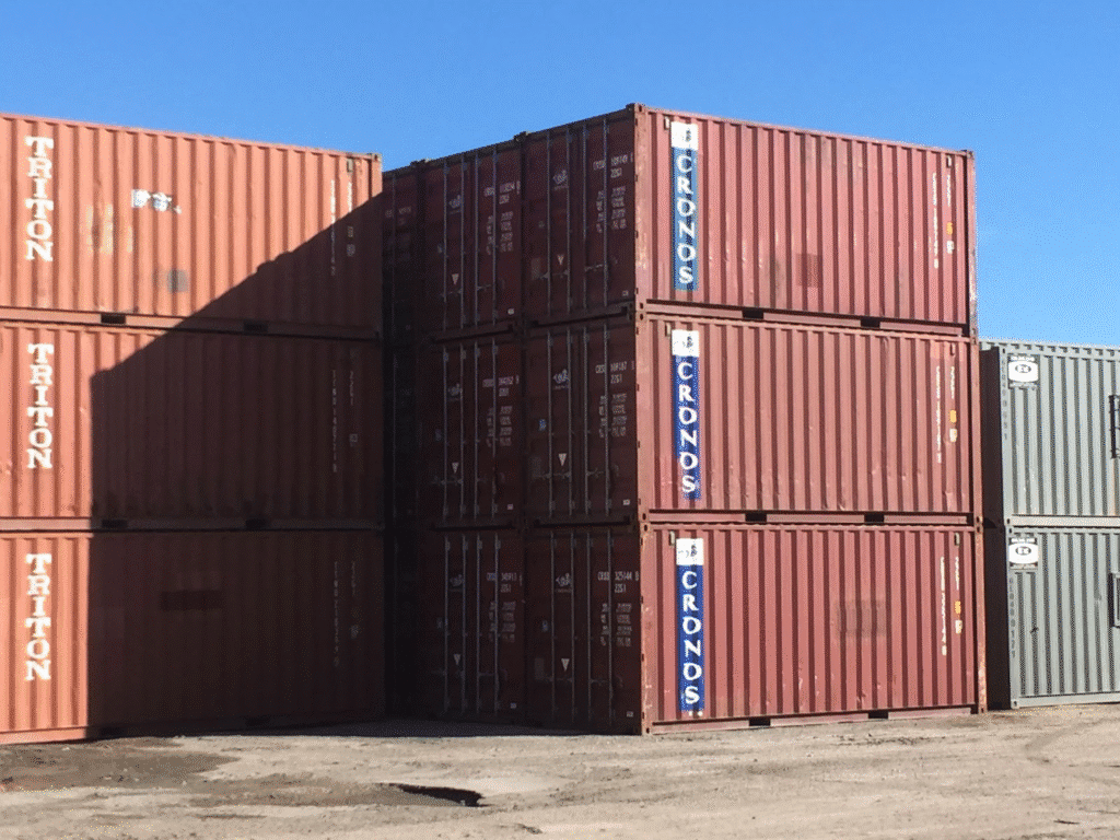 Used cargo containers in an industrial area under a clear blue sky.