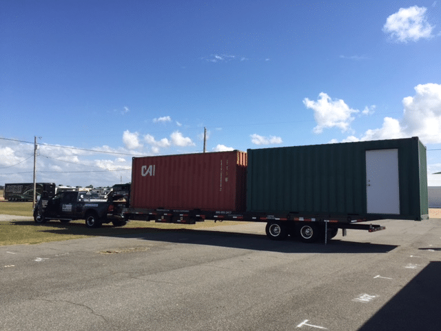 Flatbed truck transporting red and green storage containers under a blue sky.