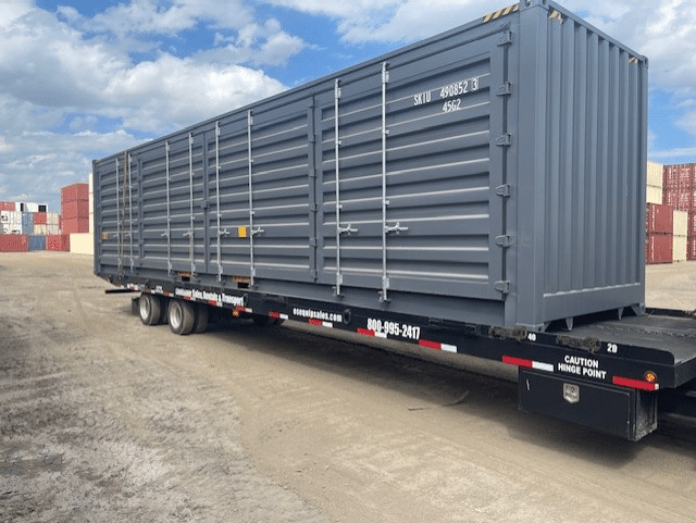 Gray shipping container on flatbed trailer at industrial yard under blue sky.