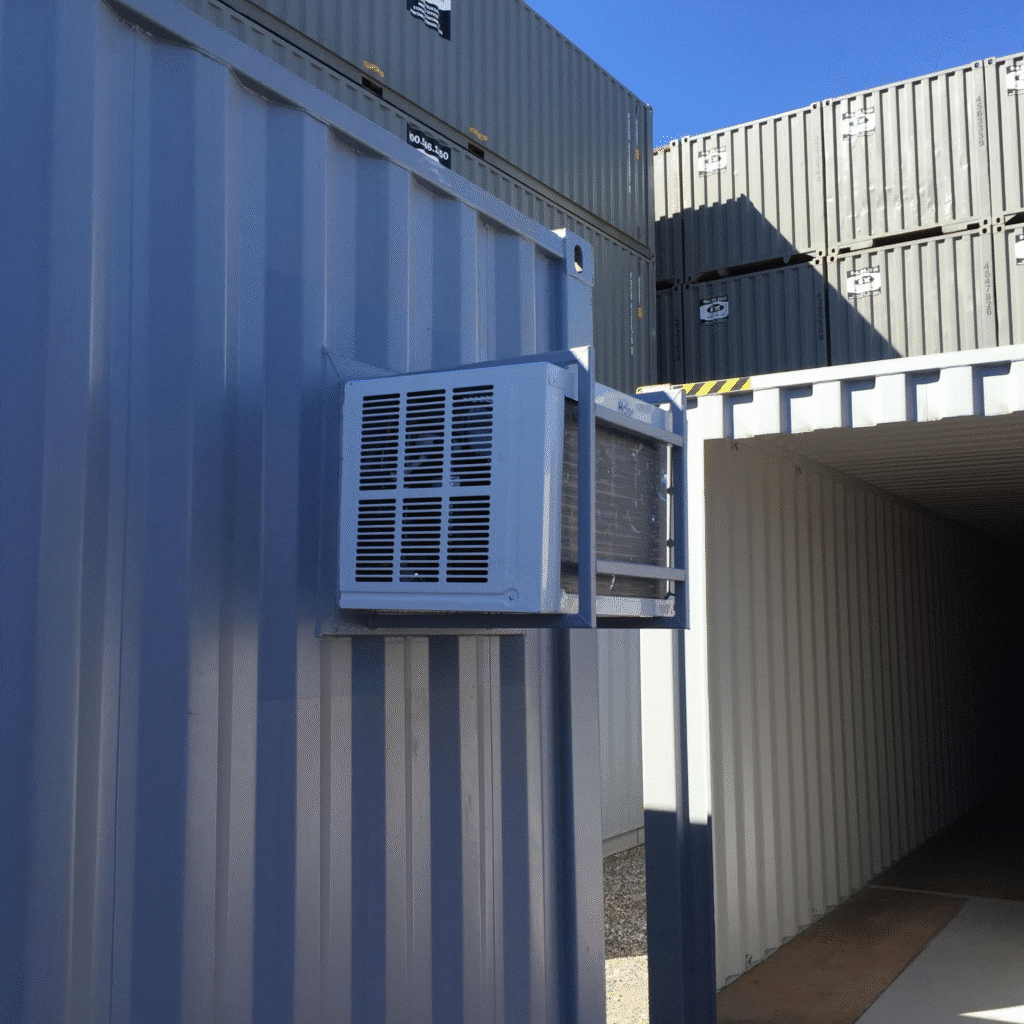 Air conditioning unit installed on a blue shipping container, with stacked containers in the background.