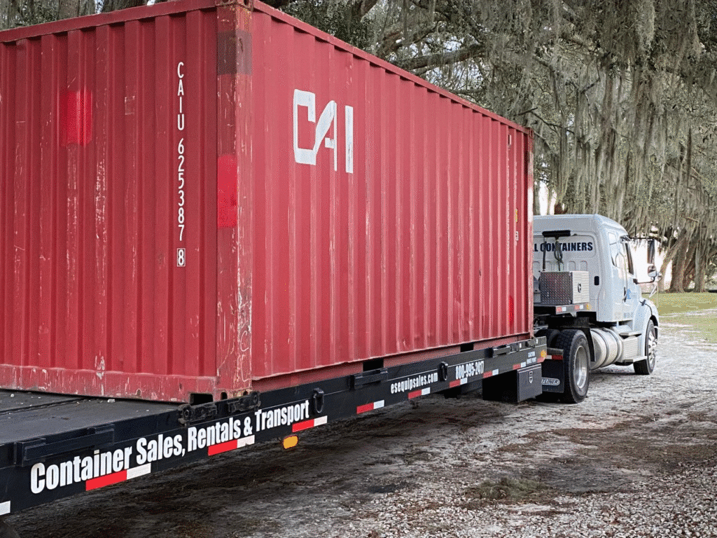 Red shipping container on flatbed truck marked for sale and transport in a wooded area.