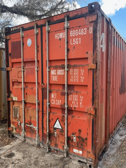 Red shipping container with visible wear, displaying weight and capacity specifications, closed and locked.