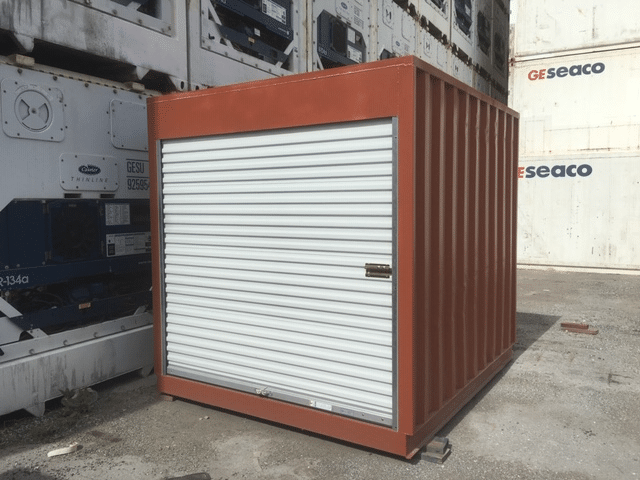 Red shipping container with white roll-up door in an industrial area.