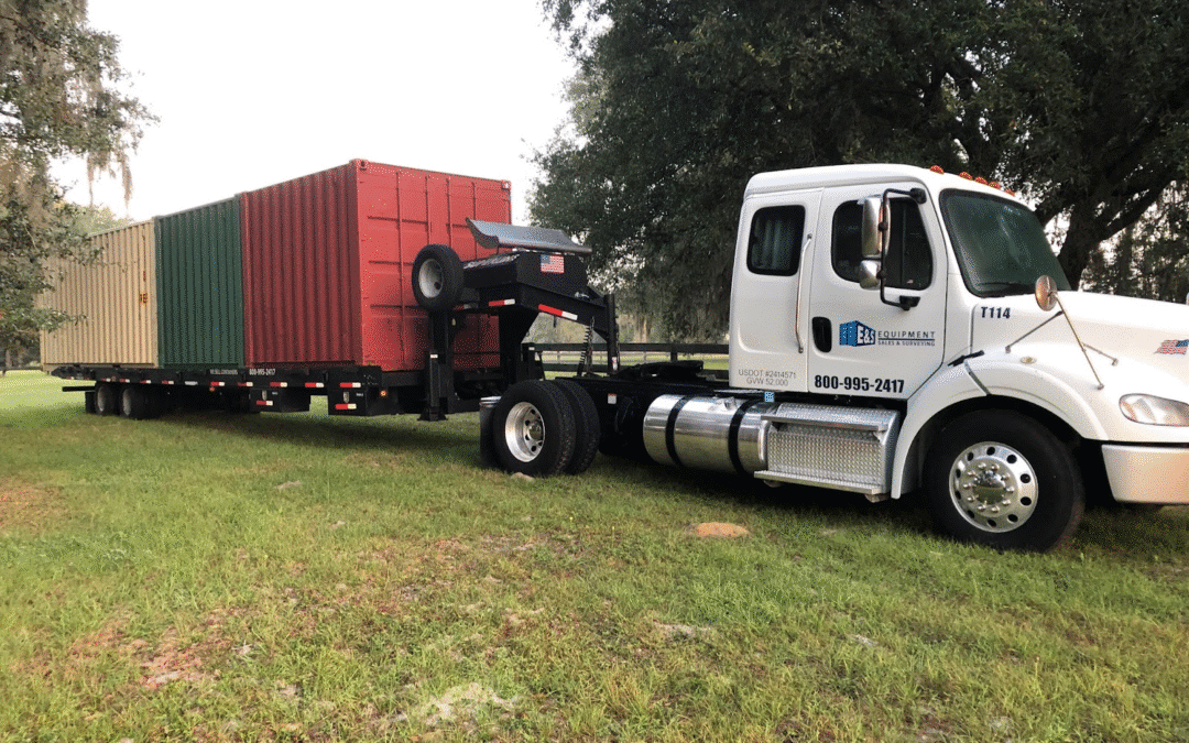Truck hauling three colorful shipping containers on a grassy field.