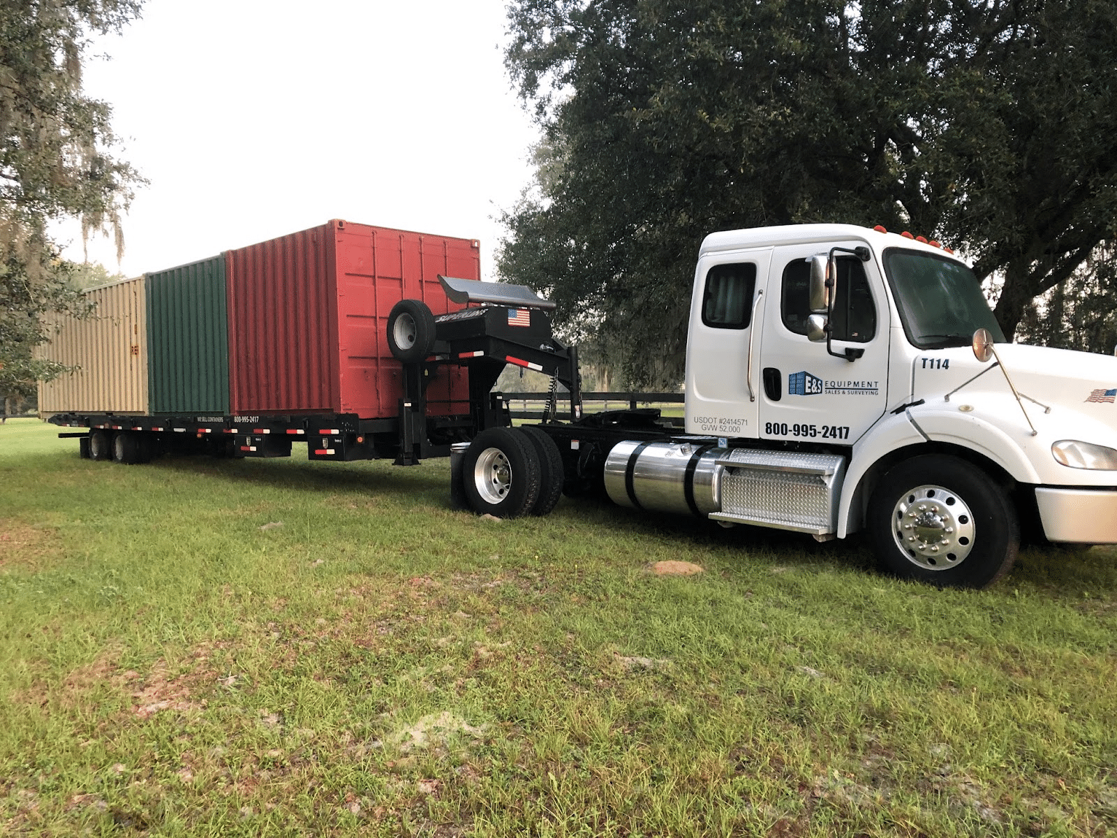 Truck hauling three colorful shipping containers on a grassy field.
