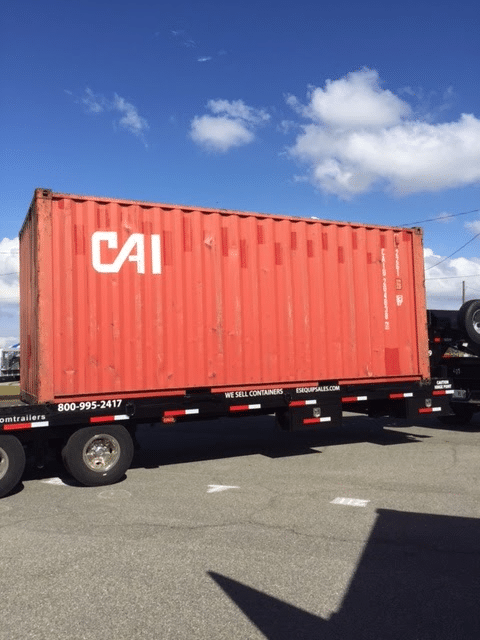 Red shipping container labeled CAI on a trailer under a clear blue sky.