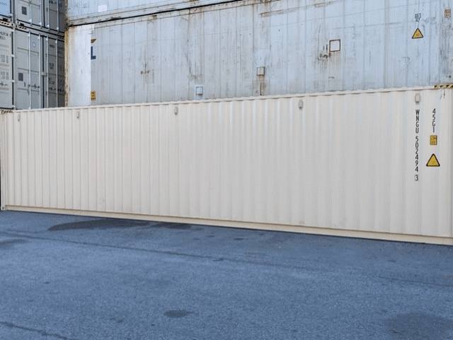 White shipping container on asphalt with other containers in the background at an industrial site.