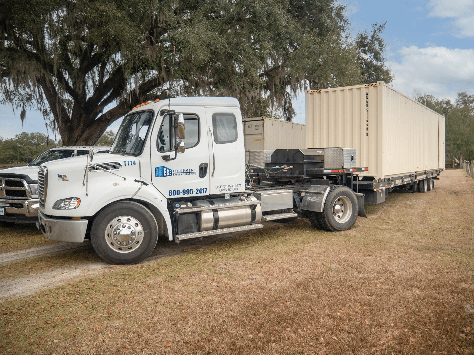 E&S Equipment Sales truck delivering a shipping container on a tilt-bed trailer in Florida
