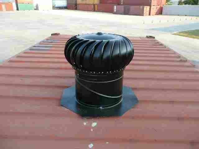 Rooftop turbine ventilator on a red metal roof in a sunny industrial area.