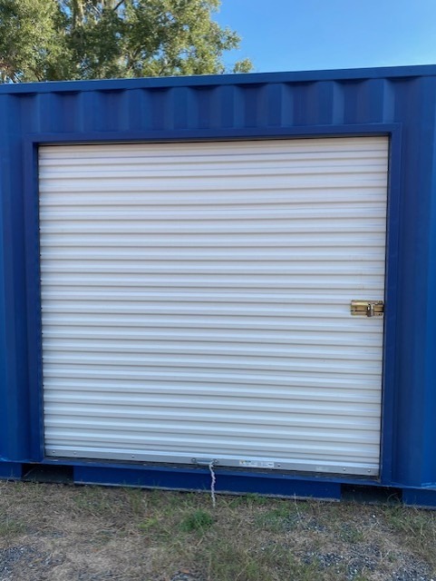 Blue storage container with a white roll-up door and padlock, outdoors on grass.