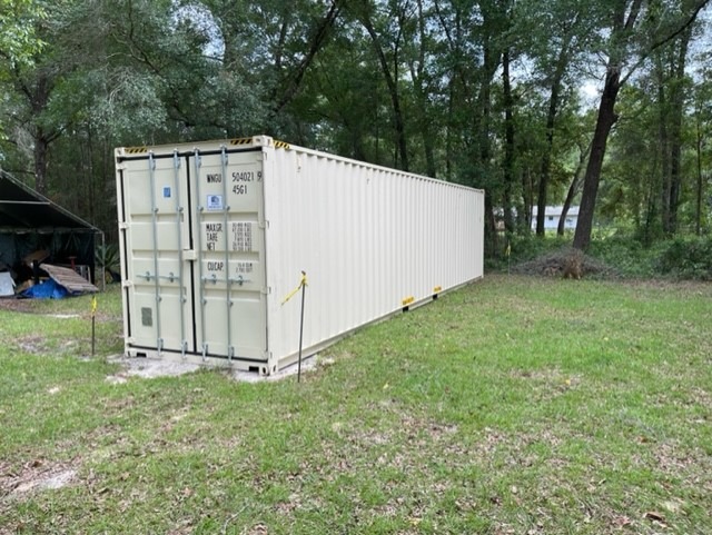 Shipping container wind resistance anchor system with steel tie-down straps bolted to concrete footing on coastal sandy soil